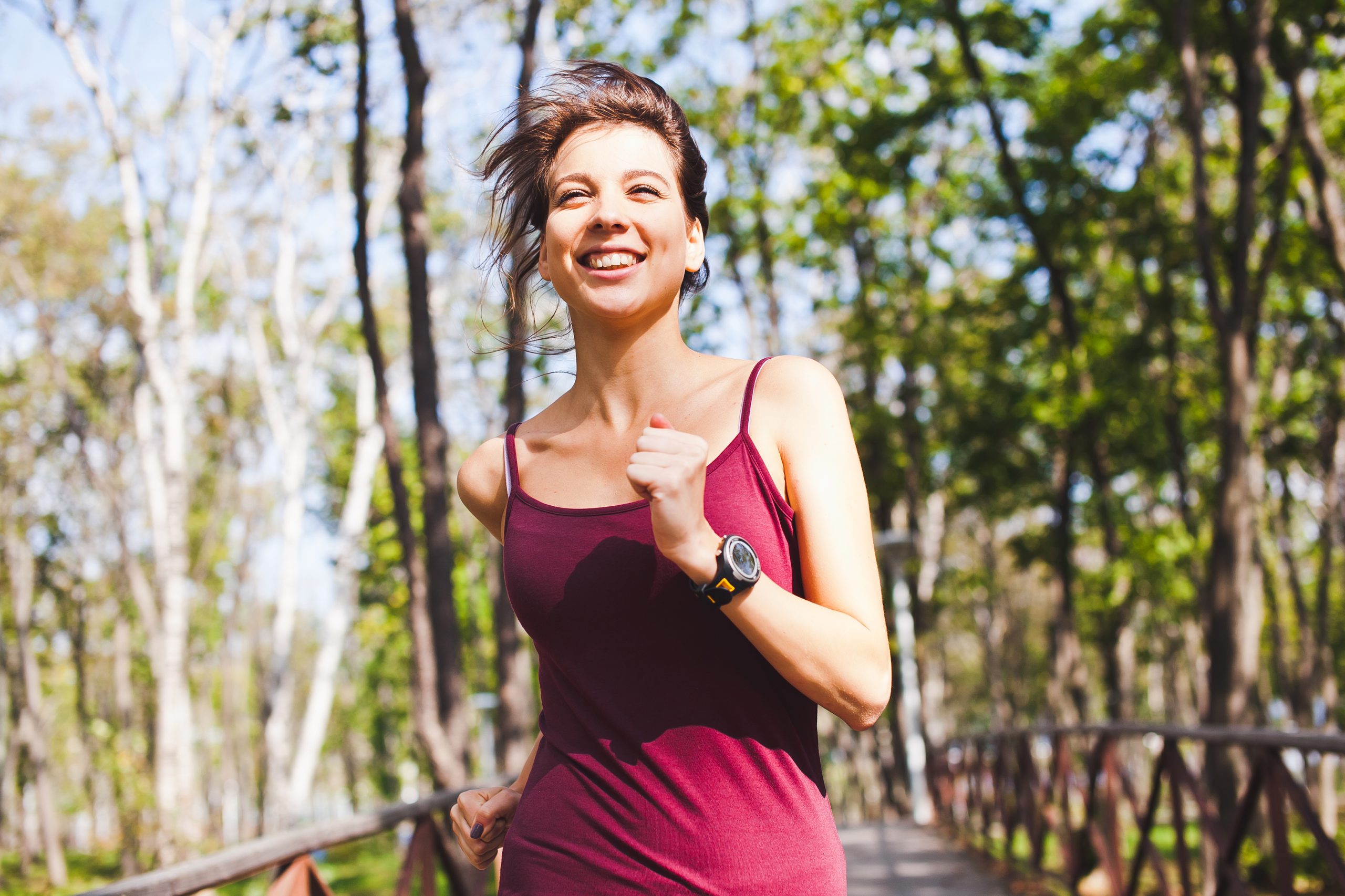 Young attractive sporty smiling woman running in forest wearing sport gadget